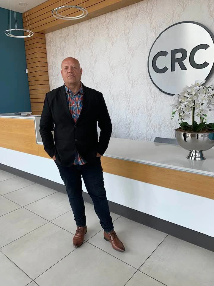 Lowell Jeffery, CRC bassist, standing beside the CRC logo at Christian Revival Church